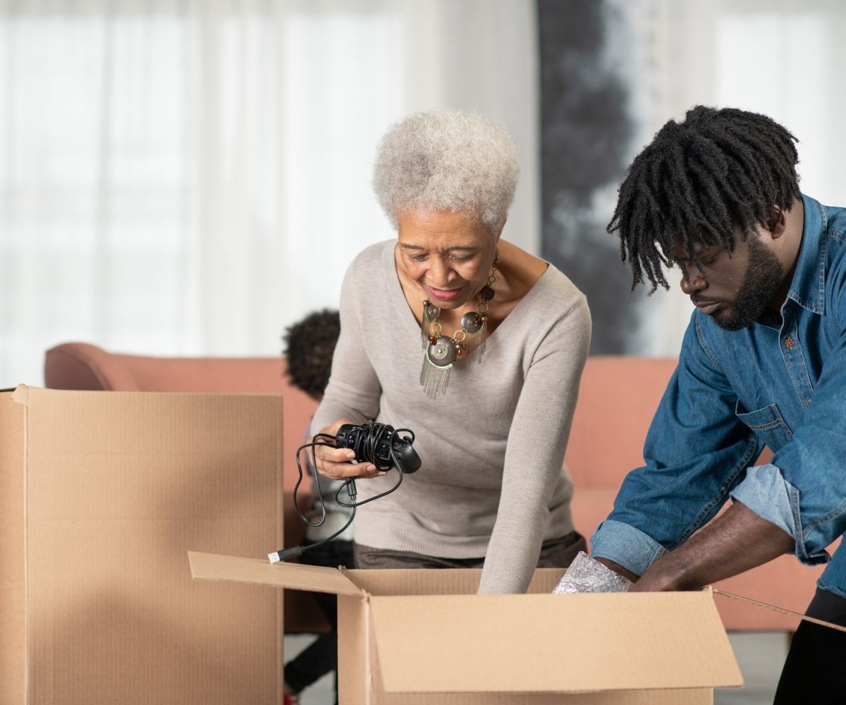An elderly woman and a man unpacking a cardboard box together in a living room.