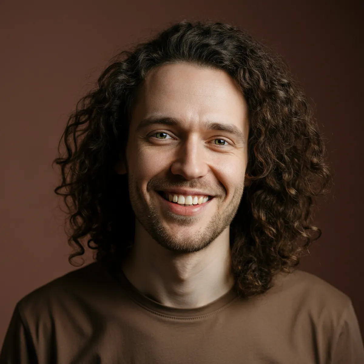 Portrait of a man with curly hair and beard smiling in warm lighting.