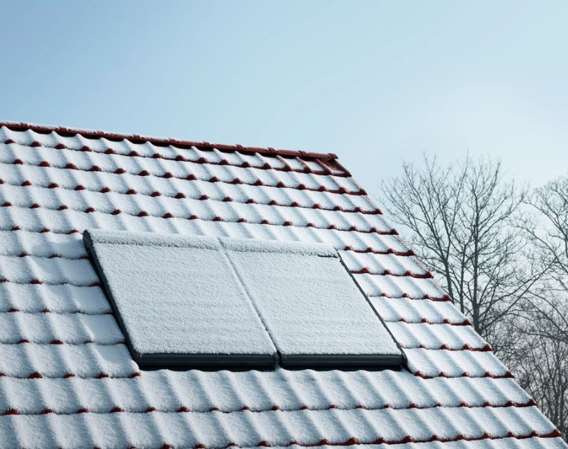 Zasněžené střešní okno VELUX osazené v klasické taškové střeše.