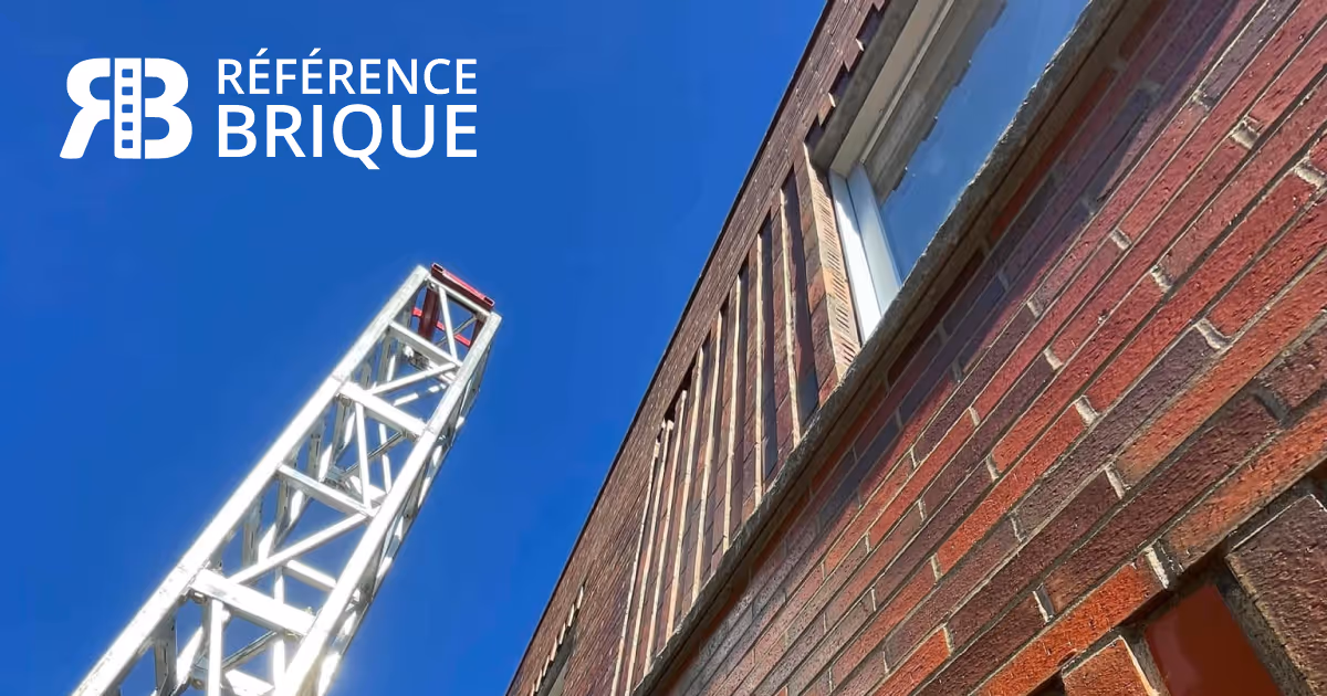 Façade en briques rouge avec fenêtre et grue métallique contre un ciel bleu, logo Référence Brique en blanc.