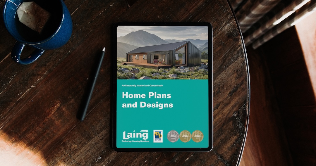 Tablet on a wooden table displaying a digital brochure cover with a modern house design against mountains and text 'Home Plans and Designs' with Laing logo and awards.