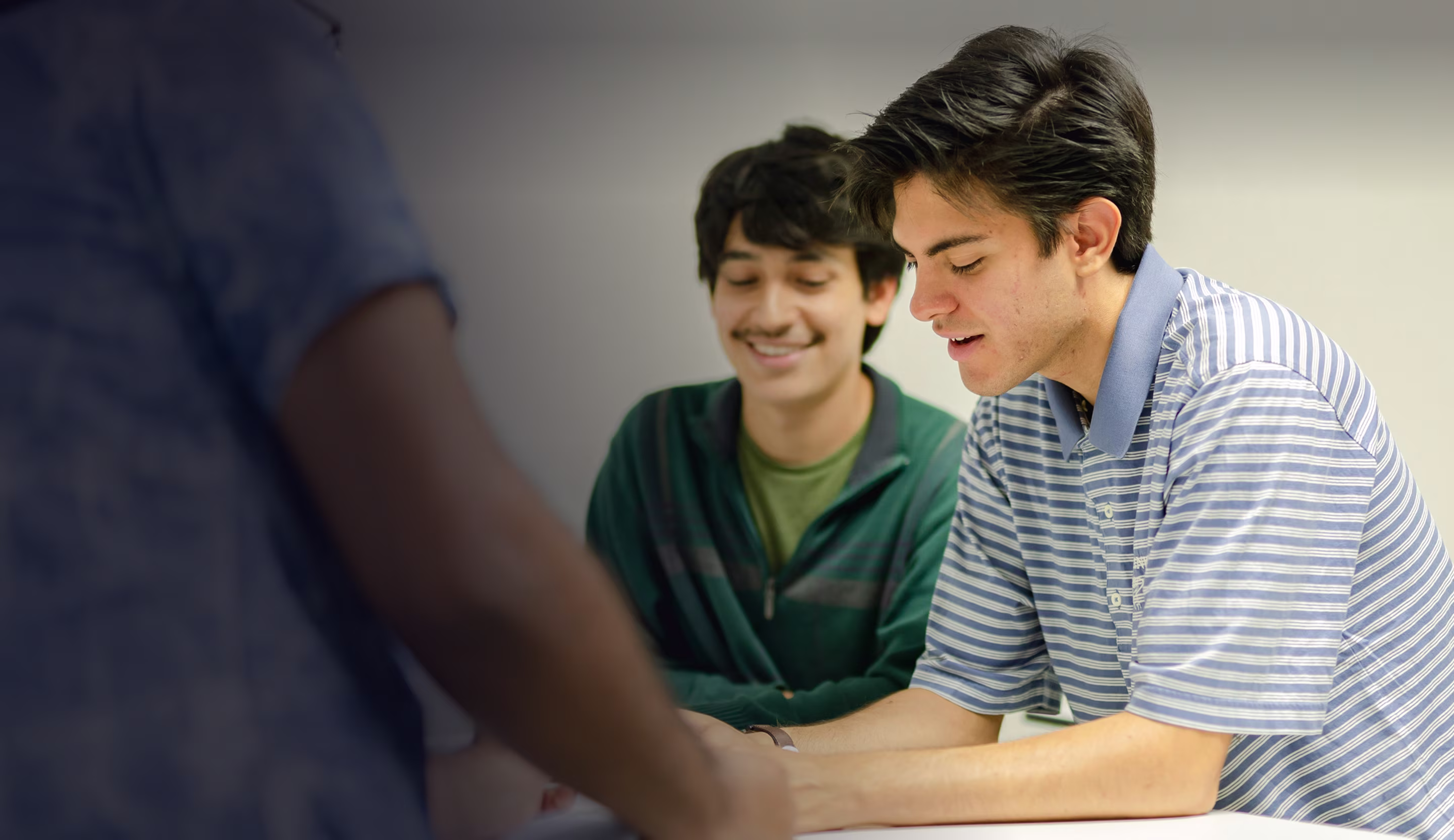 Three young men engaged in a collaborative discussion around a table.