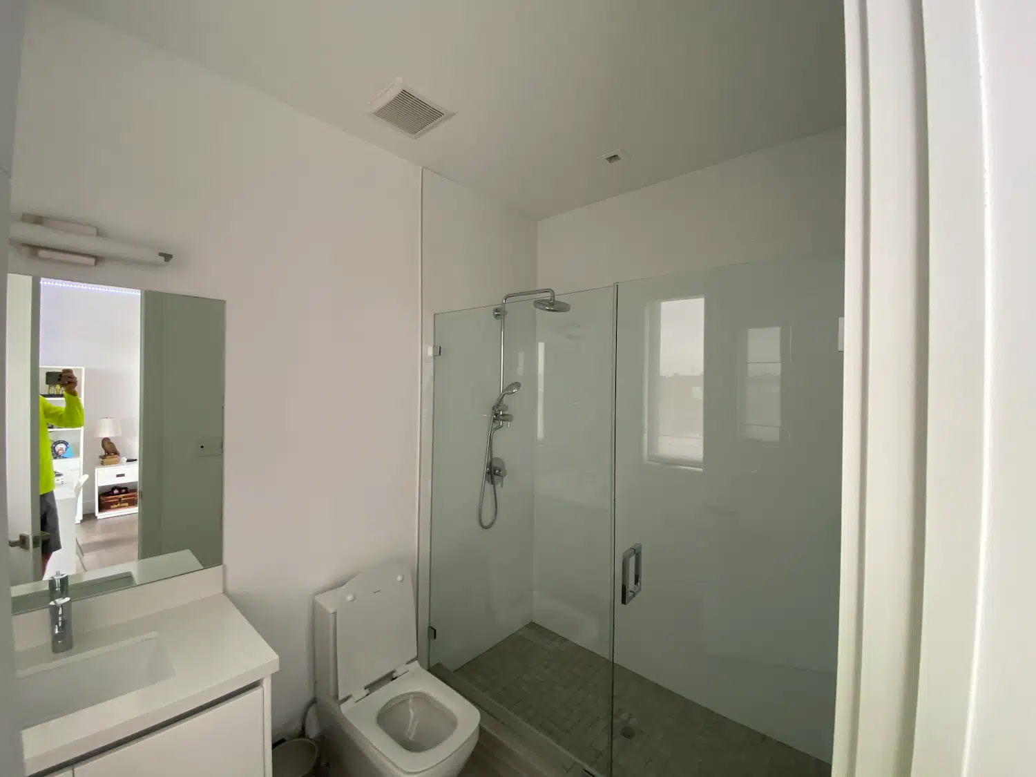 Guest bathroom before remodeling in Weston, FL, with white walls, a white vanity, rectangular mirror, and glass-enclosed shower.