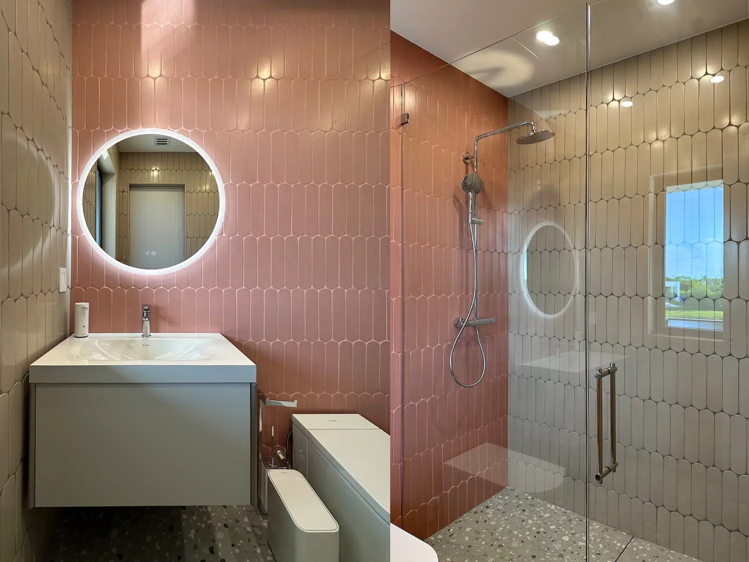 Guest bathroom after remodeling in Weston, FL, with pink and beige tile, a floating vanity, round LED mirror, and frameless glass shower.