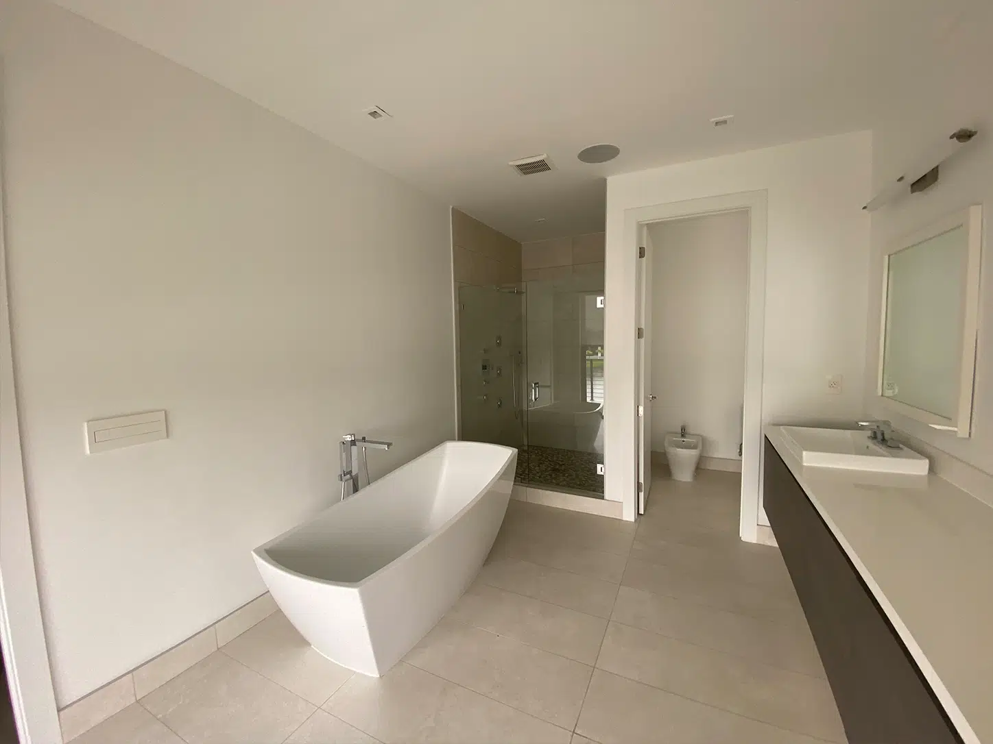 Remodeled bathroom in Weston, FL, with blue cabinetry, gold fixtures, a freestanding tub, leaf-pattern walls, and a backlit mirror.