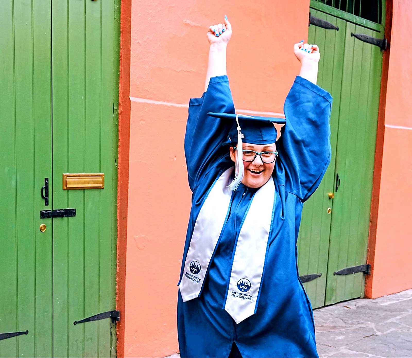 UNO College Graduate excited with arms up and smiling