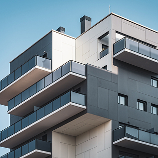 Modern apartment building with multiple glass balconies against a clear blue sky.