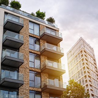 Modern apartment buildings with glass balconies and rooftop greenery under a cloudy sky with sunlight.