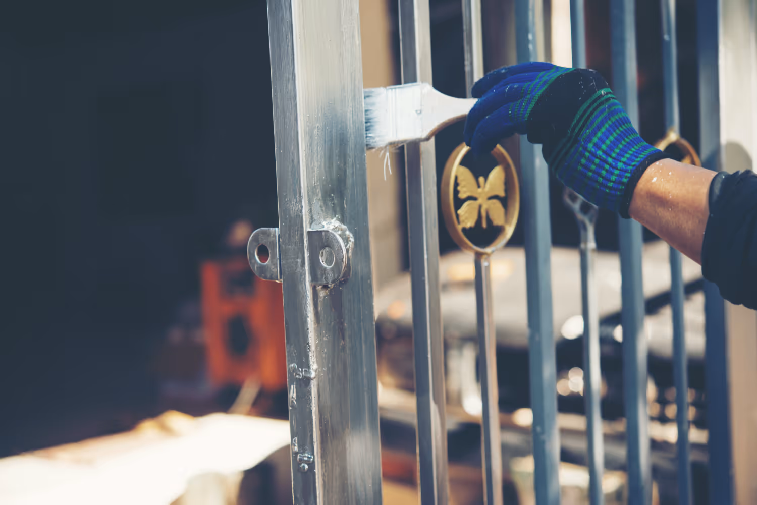 Person wearing blue and green gloves painting a metal gate with a brush.