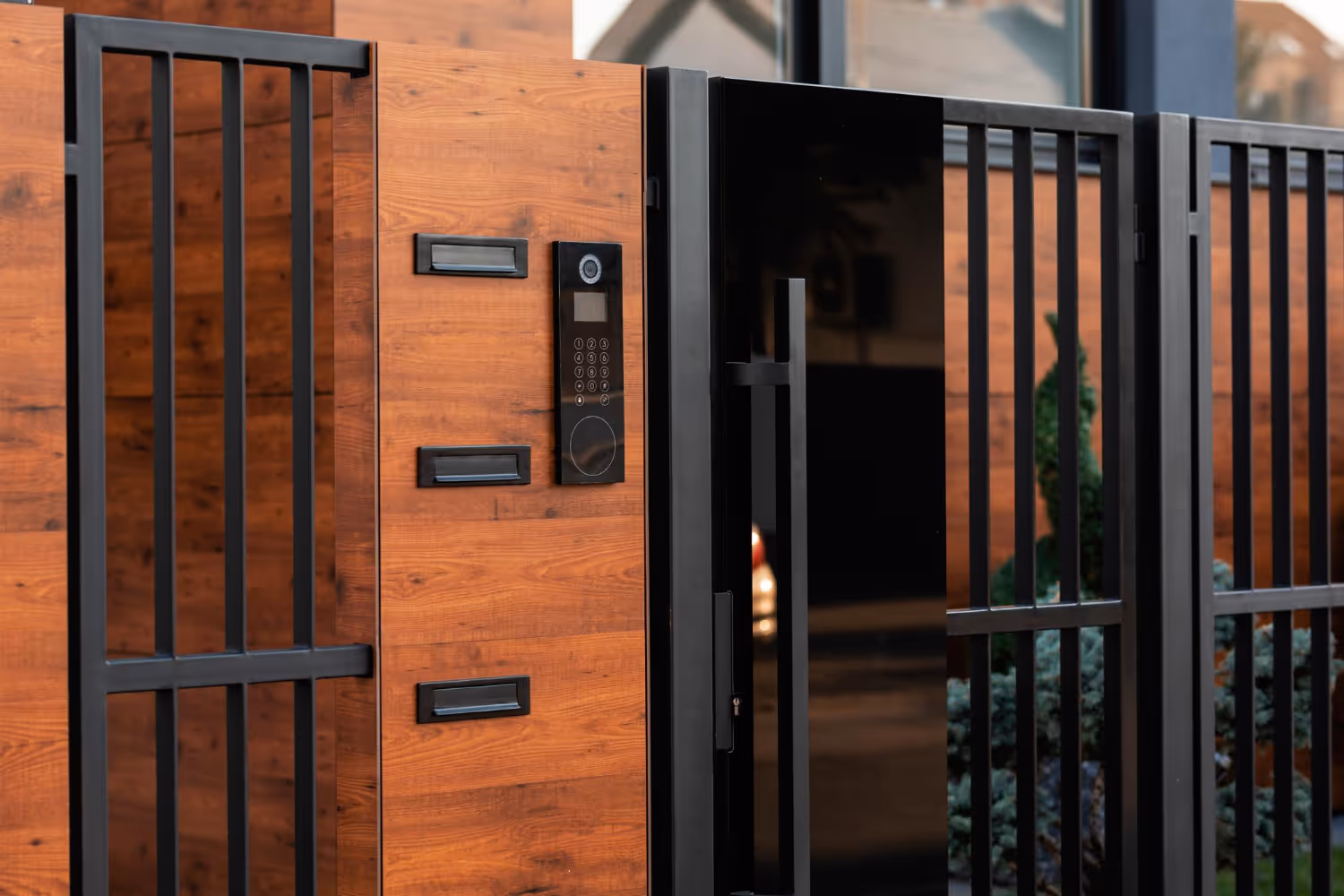Modern wooden and black metal gate featuring a keypad entry system and a large vertical handle.