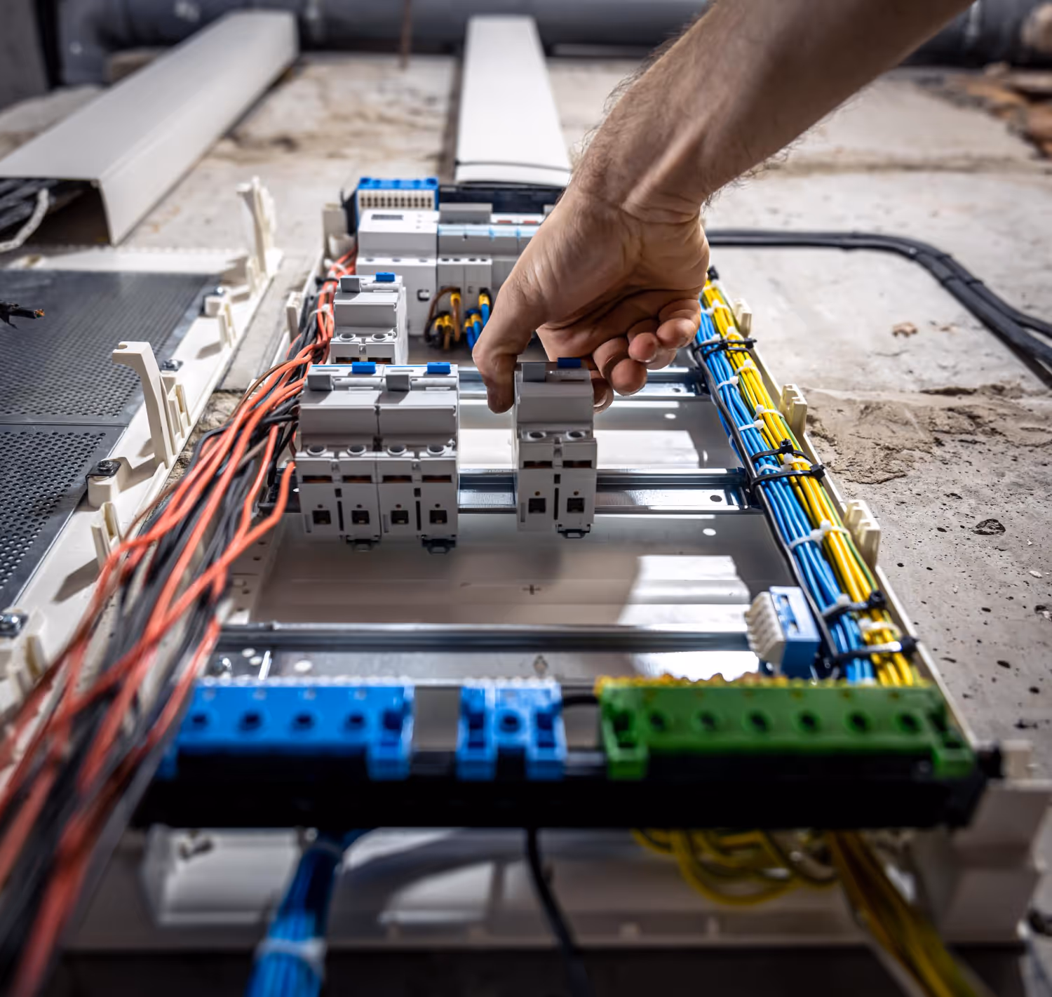 Close-up of a hand adjusting circuit breakers inside an open electrical panel with organized colored wiring.