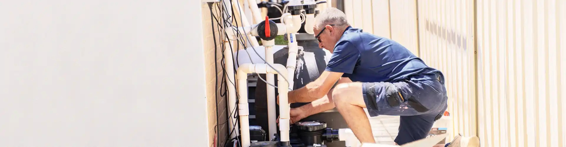 Man in red shirt and cap cleaning the edge of a pool outdoors.