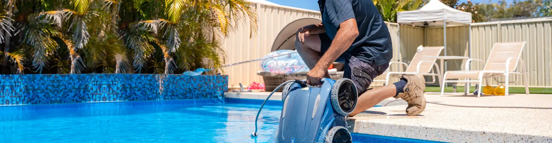 Man in red shirt and cap cleaning the edge of a pool outdoors.