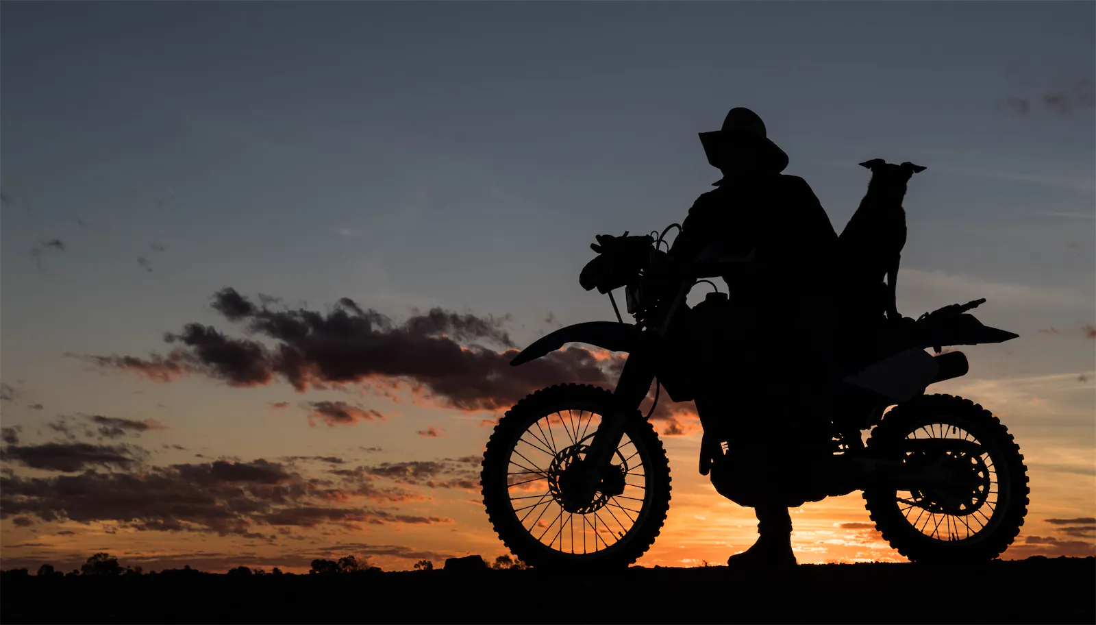 A farmer with his motorcycle and his dog at sunset