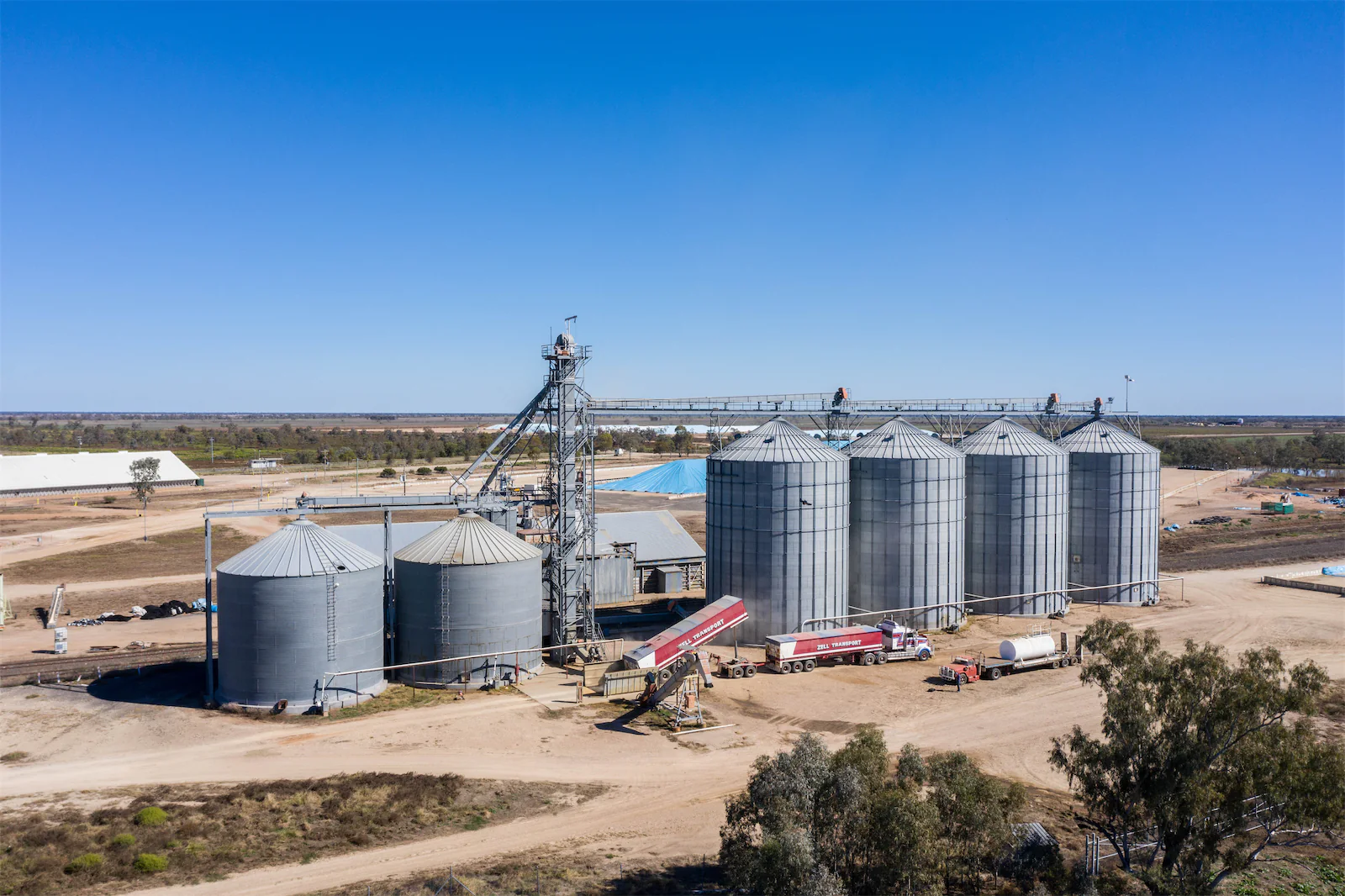 A grain storage site with large silos being filled with grain.