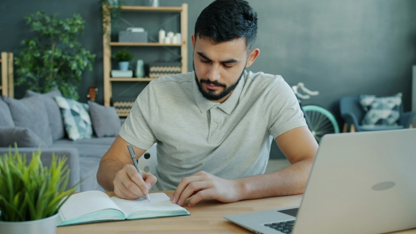 Adult writing notes at a desk at home, next to a laptop