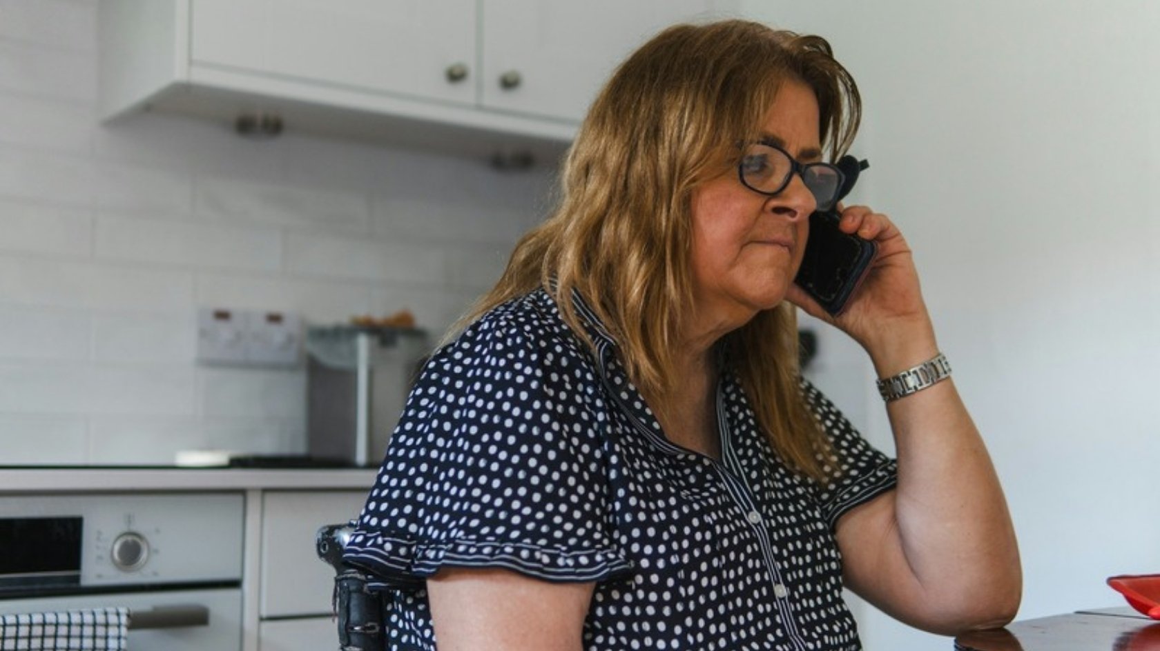 Woman on the phone at her kitchen table, trying to book a GP appointment