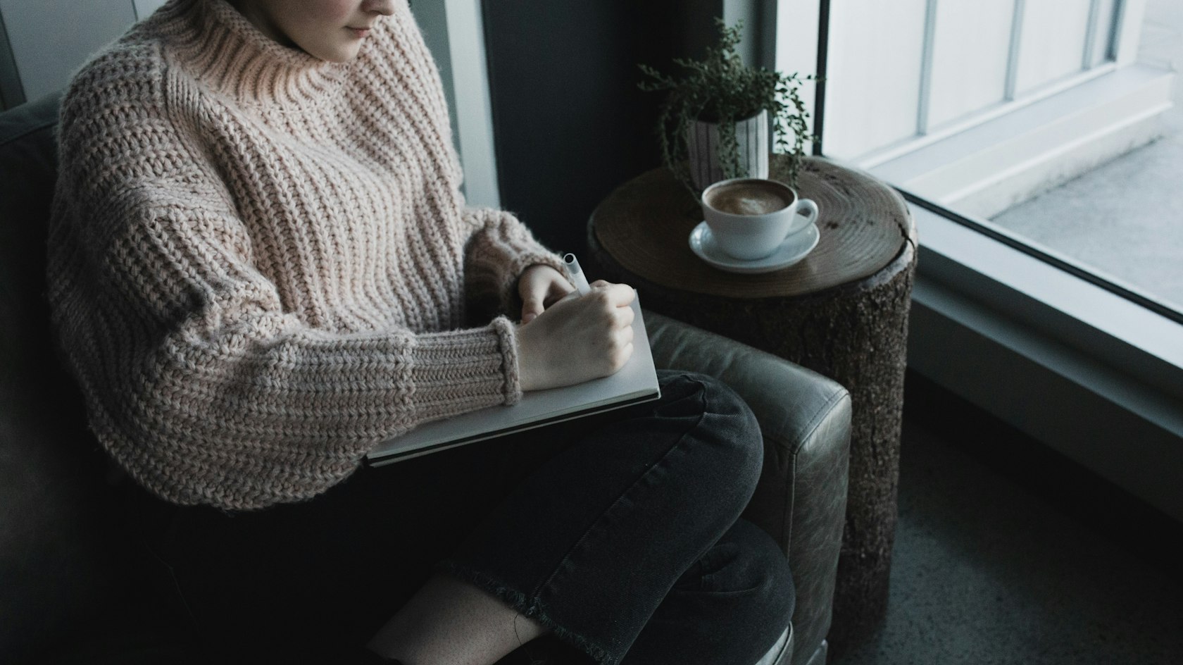 Woman writing in a notebook in an armchair by a window