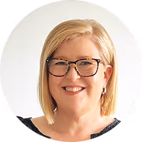Smiling middle-aged woman with blonde hair and black-framed glasses against a white background.