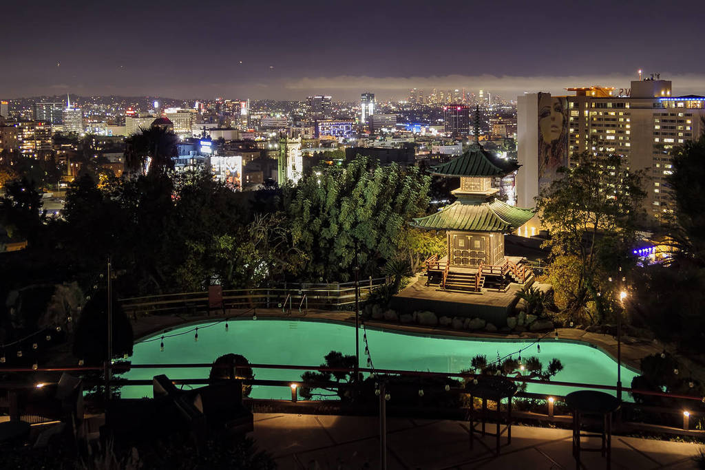 View over LA skyline at night with Japanese pagoda and swimming pool in the foreground.