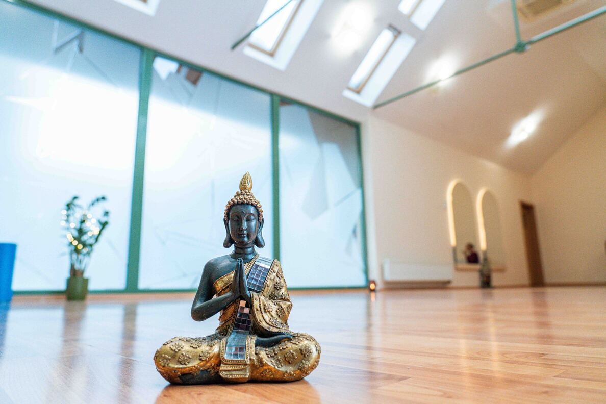 Soška sediaceho Budhu s rukami v modlitbe na lesklej drevenej podlahe v jasnej joga miestnosti.