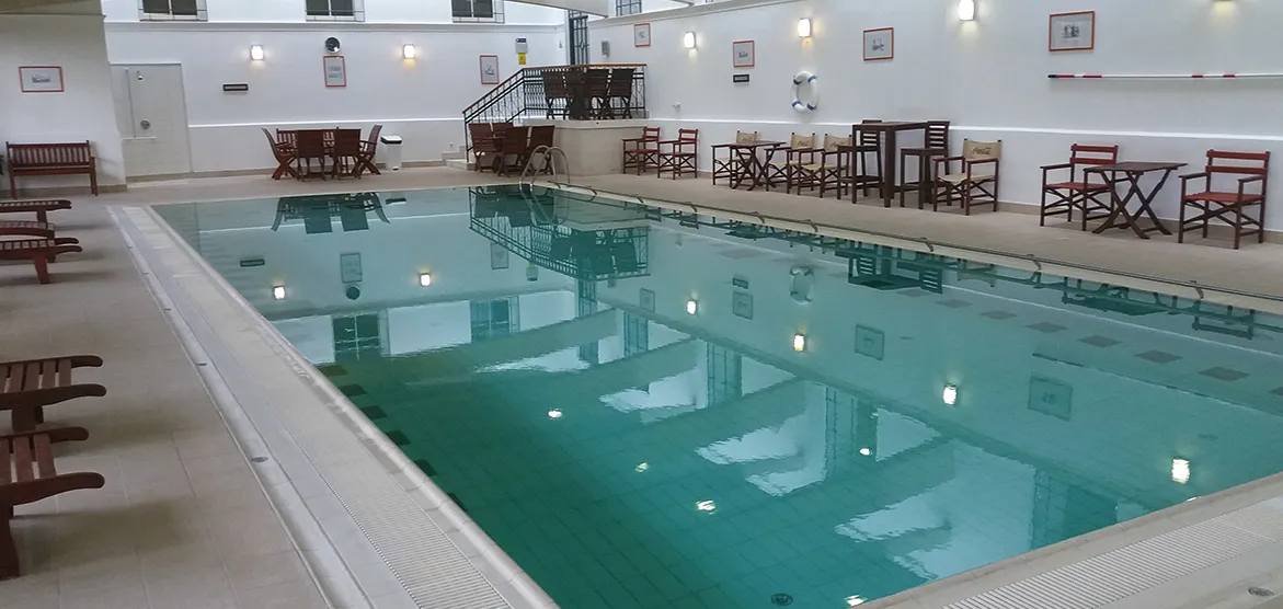 Vnútorný plavecký bazén so stoličkami, stolmi a obrazmi na stenách v priestrannej miestnosti.