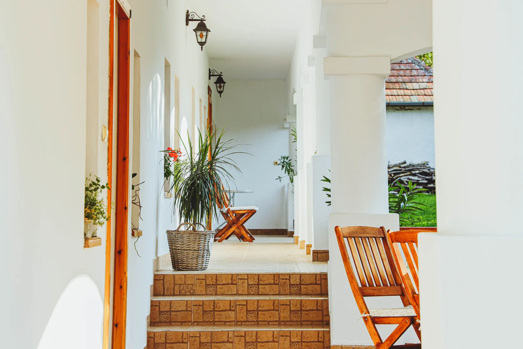 Krytá veranda s drevenými stoličkami, kvetináčmi a dlažbou so vzorom v tehlovej farbe.