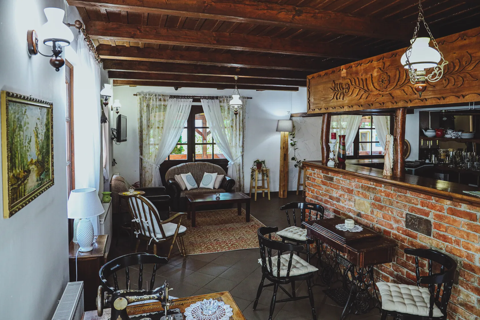 Rustikálne zariadená obývacia izba s dreveným stropom, tehlovým barom, starožitným šijacím stolom a pohodlným sedením pri okne.