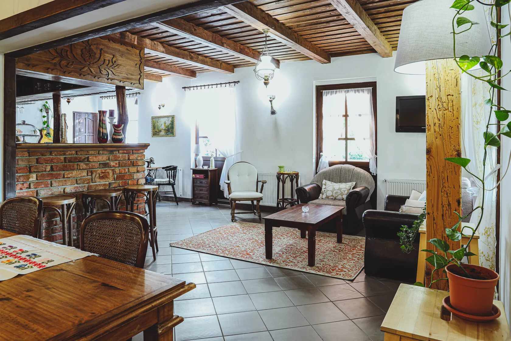 Rustikálny obývací priestor s dreveným stropom, čalúnenými kreslami, dreveným stolíkom, tehlovým barom a rastlinou v kvetináči.