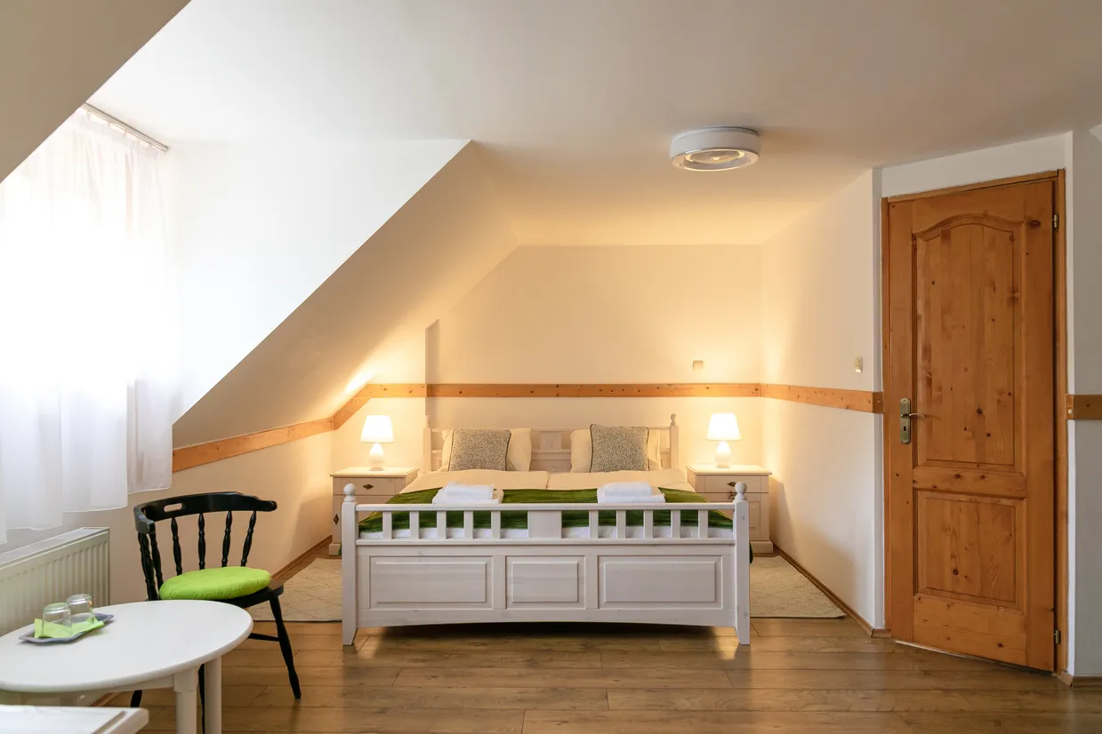 Útulná spálňa s bielou posteľou, dvoma nočnými stolíkmi so zapnutými lampičkami a drevenými detailmi.