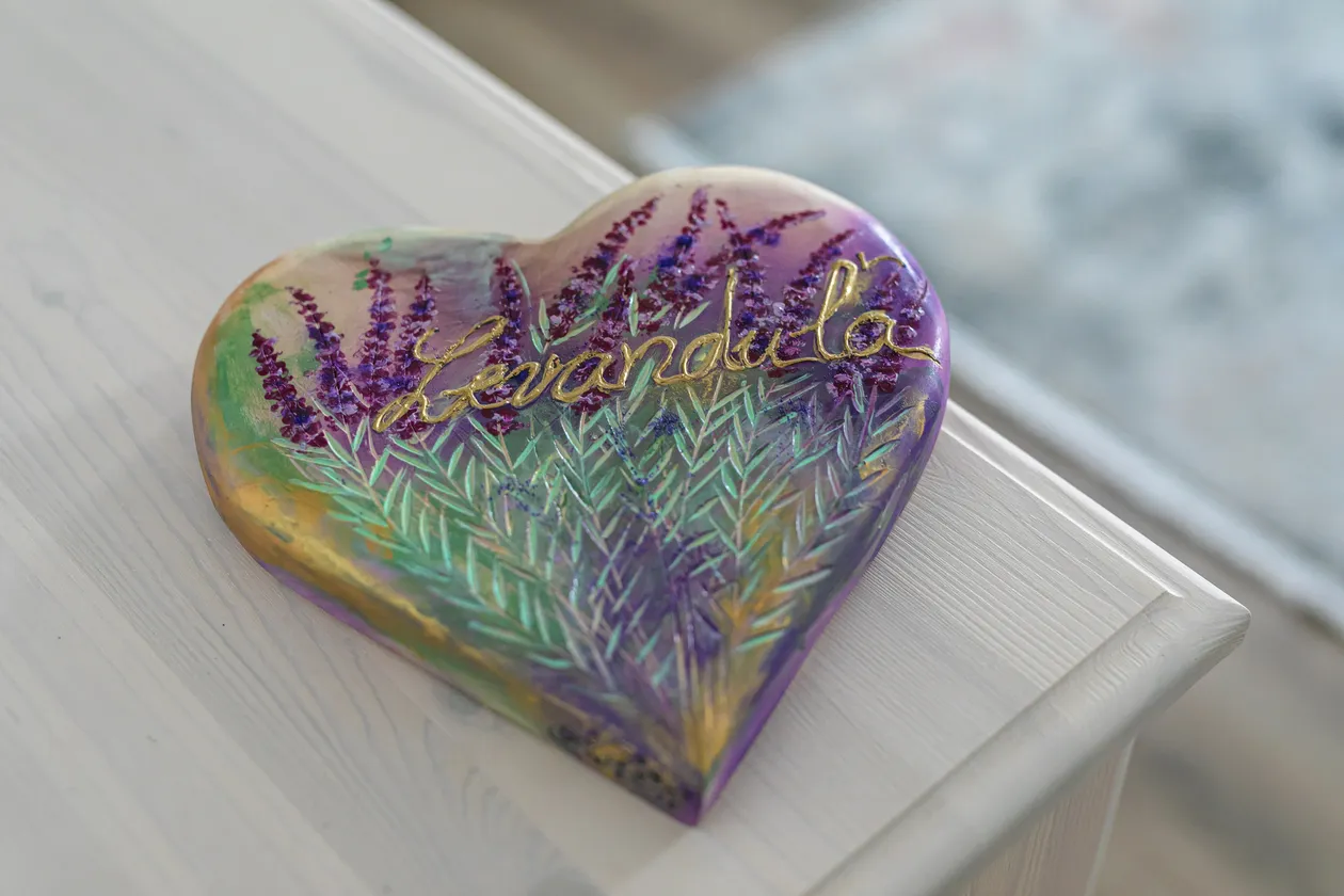 Srdce s maľbou levandule a nápisom „Levanduľa“ v zlatej farbe na bielom drevenom stole.