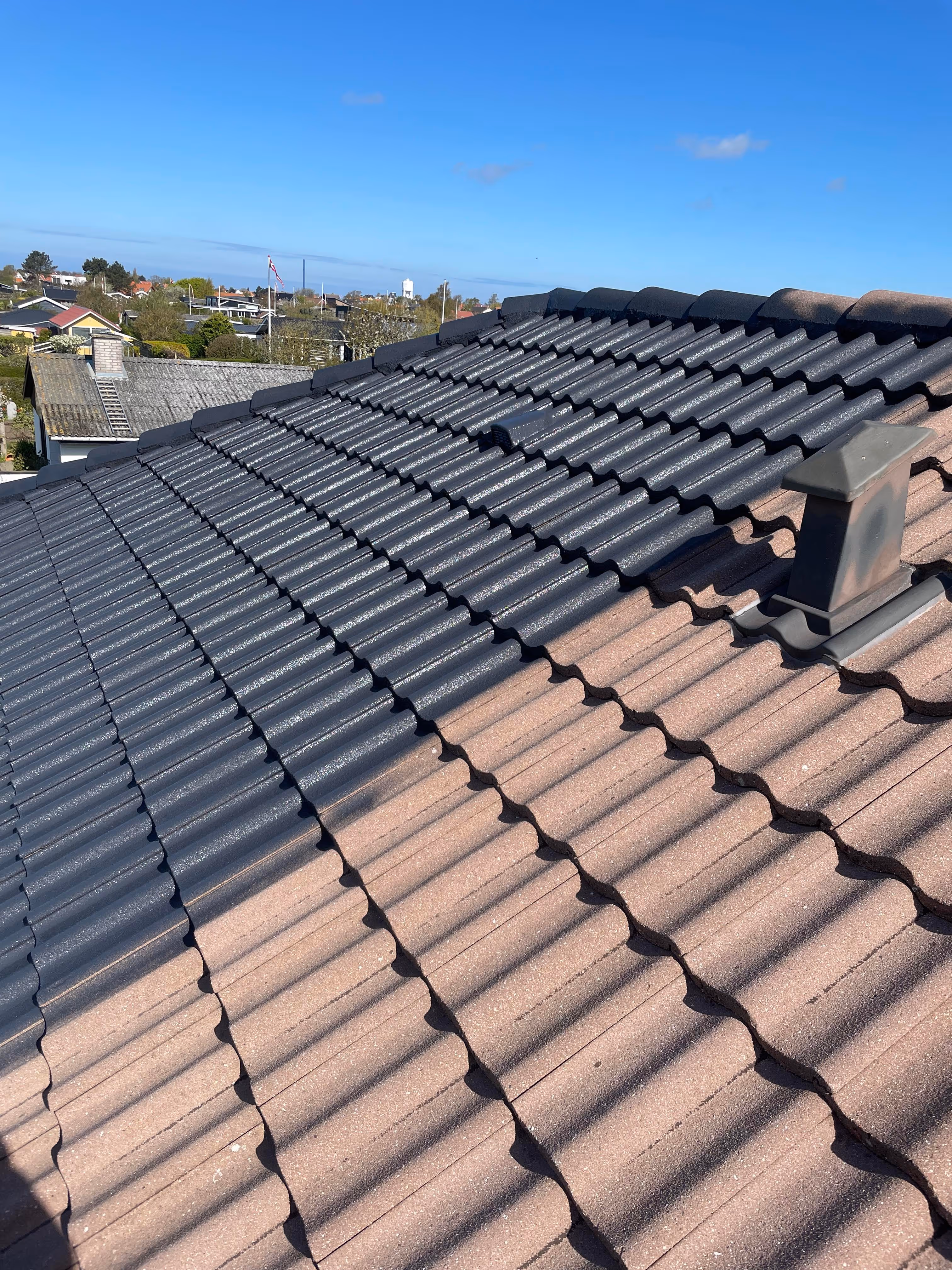 Tag med delvist malede tagsten fra brun til grå under en klar blå himmel.