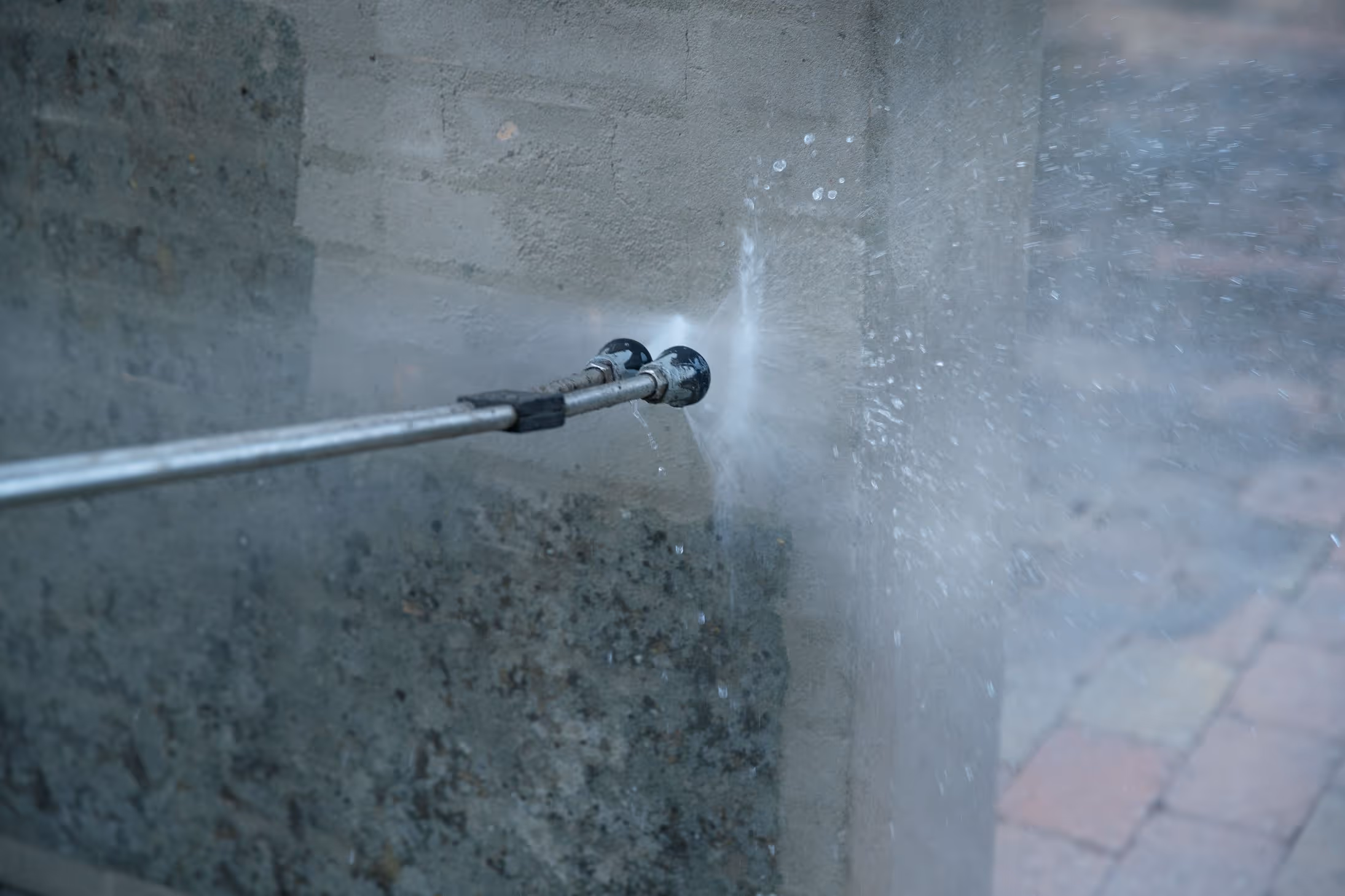 Højtryksrensning af en betonmur med synlige vanddråber og rengjort område.