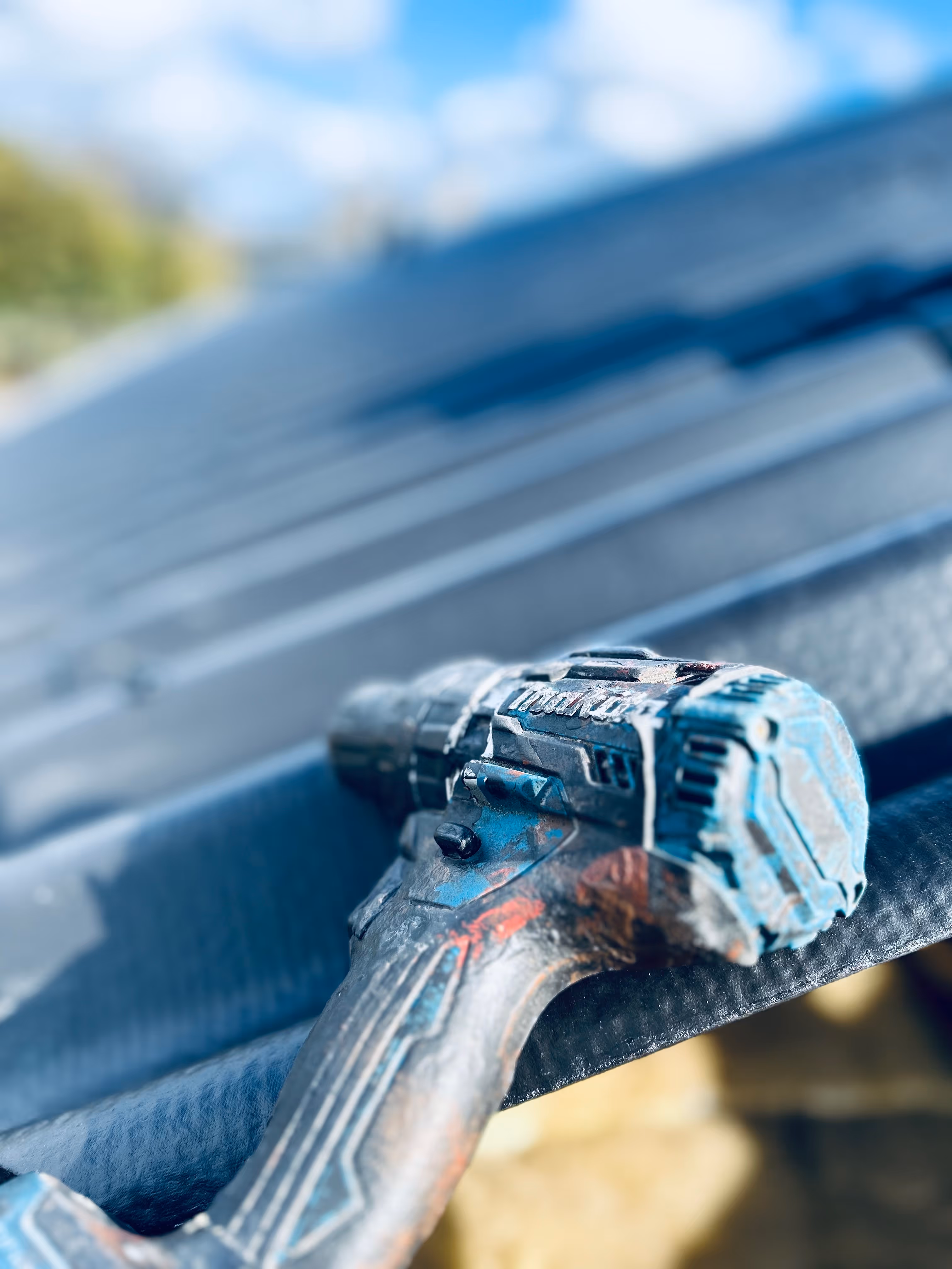 Elektrisk skruetrækker med blå og sort håndtag lagt på nyt b6 tag udendørs.