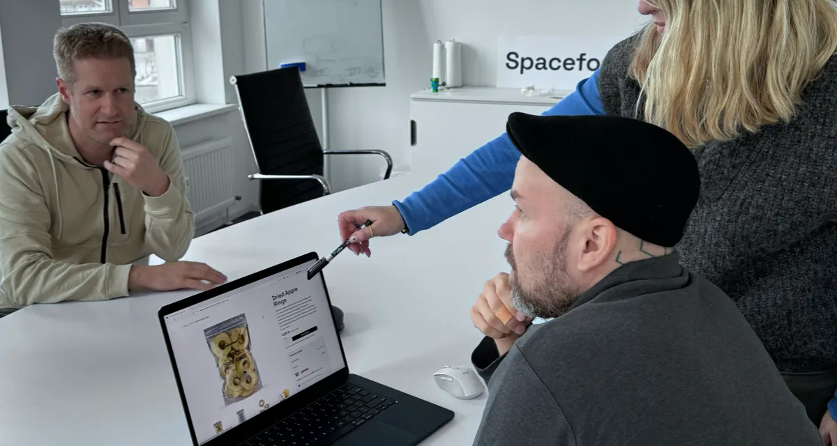 Three people in a modern office evaluating design details of a project on a laptop screen.