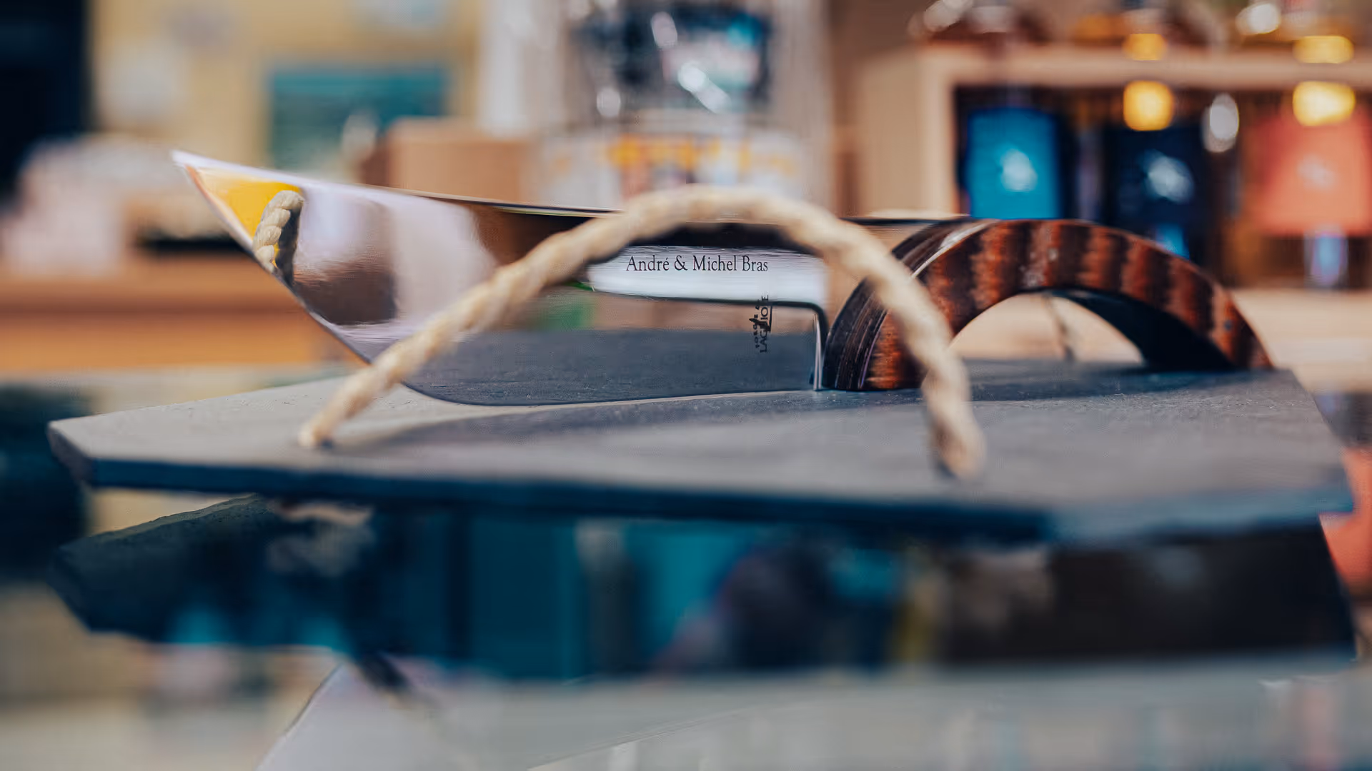 Un couteau de cuisine avec une lame en acier brillant et un manche en bois, posé sur une surface grise avec un cordon en corde devant.