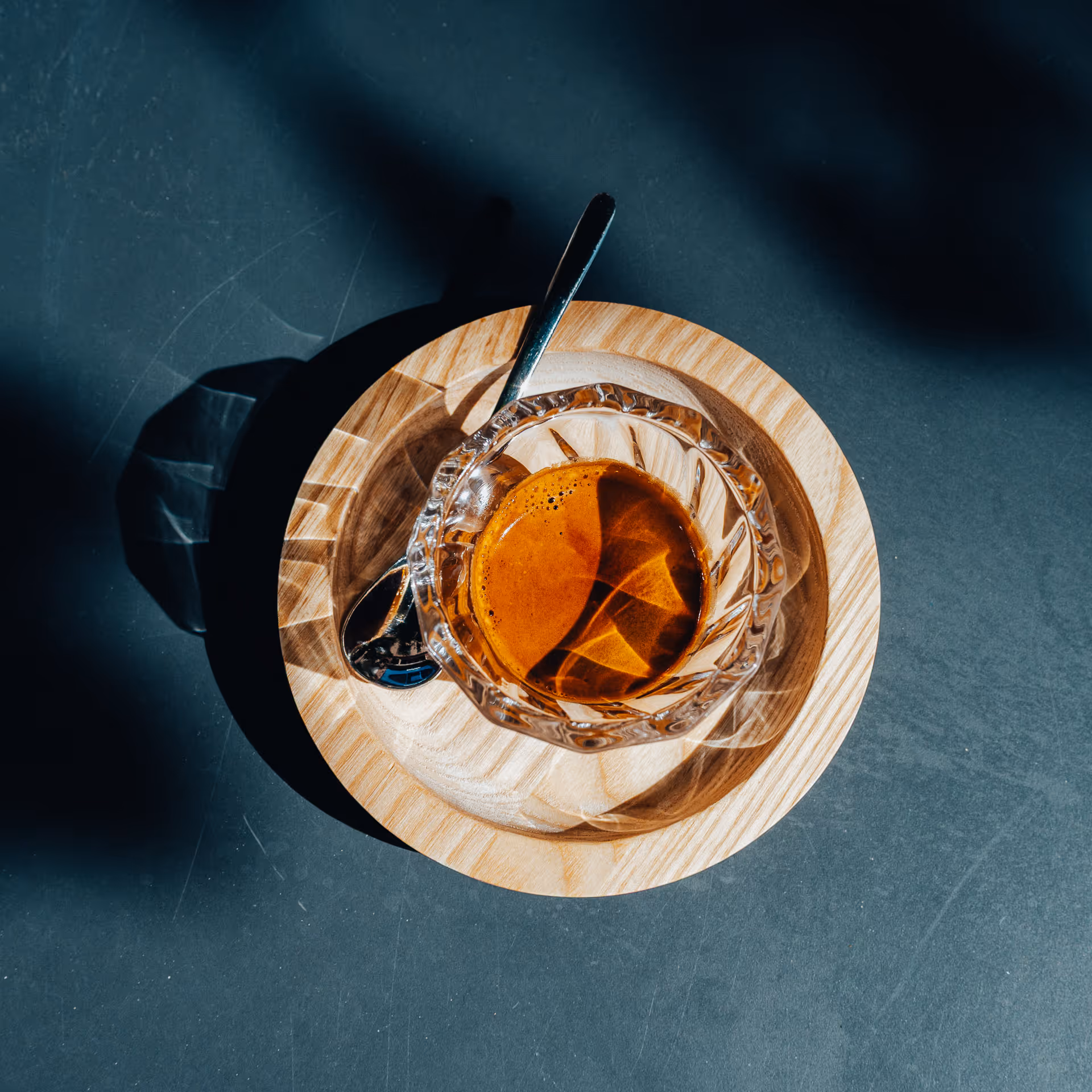 Tasse de café espresso dans une tasse en verre facettée sur une soucoupe en bois avec une cuillère métallique.