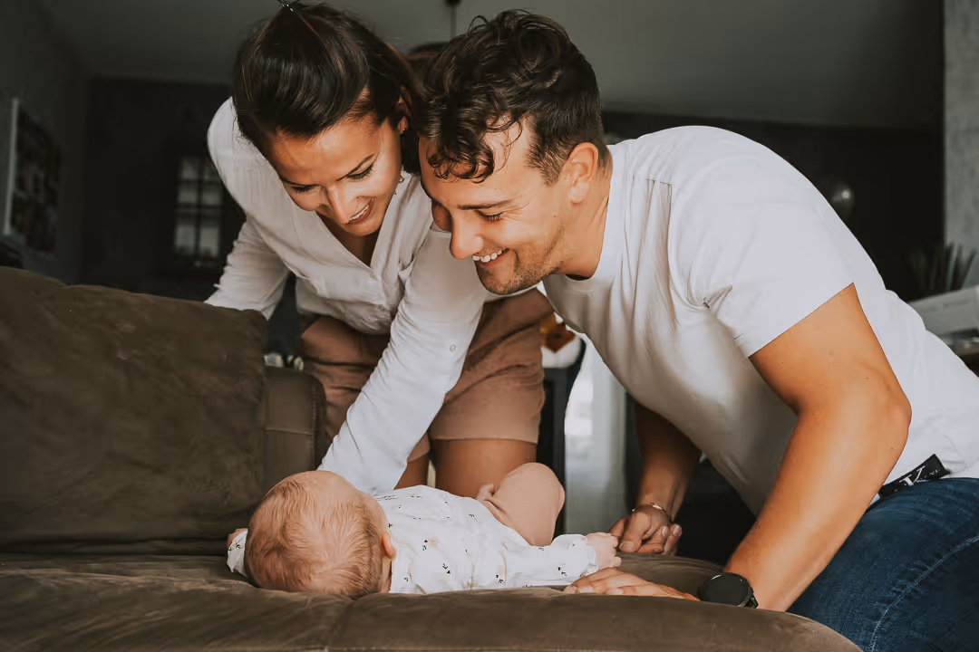 Un couple souriant regarde leur bébé allongé sur un canapé dans un salon.