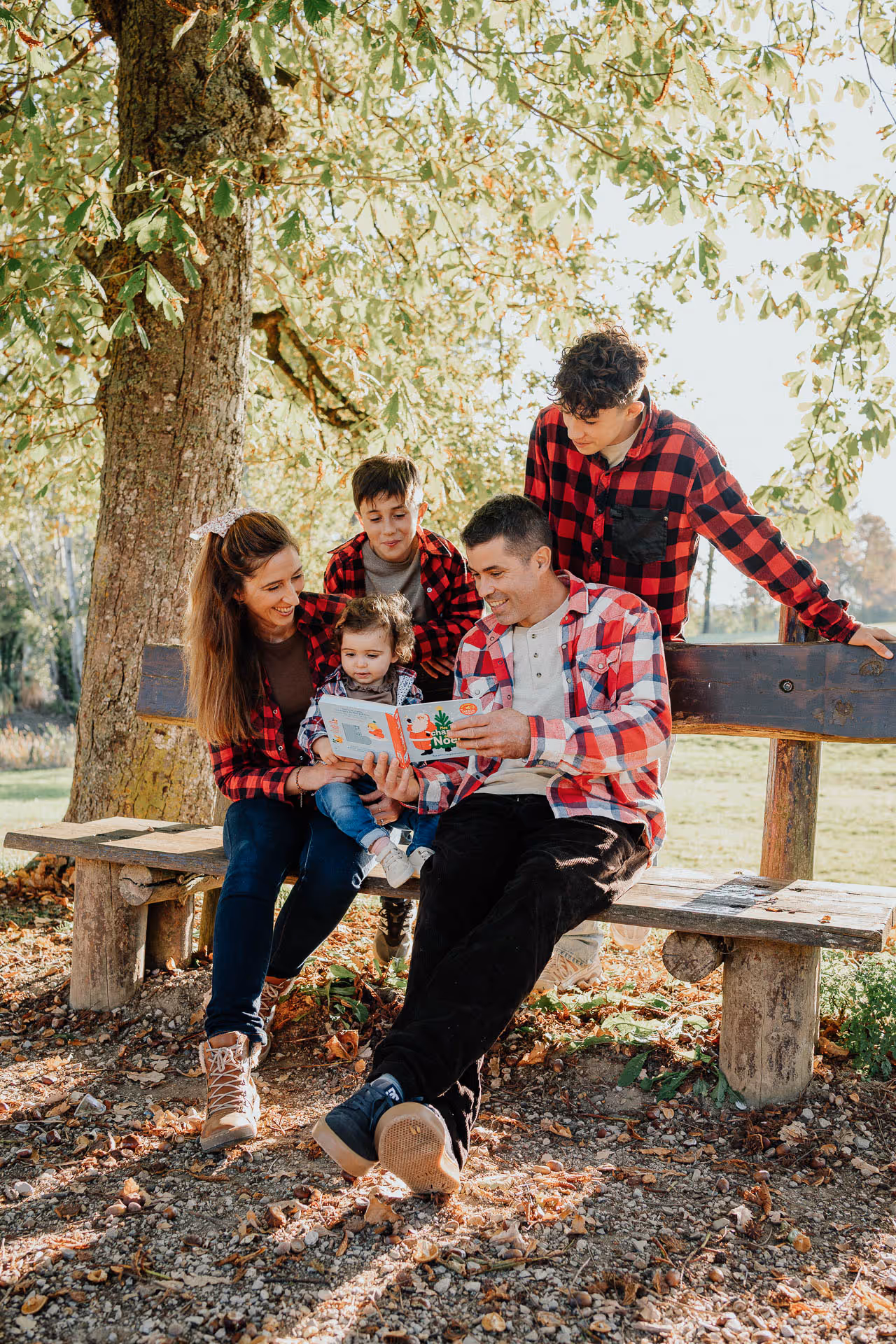 Une famille de cinq personnes en tenues blanches se tient sur un chemin campagnard, avec les parents s'embrassant au centre et leurs trois enfants les regardant avec sourire.