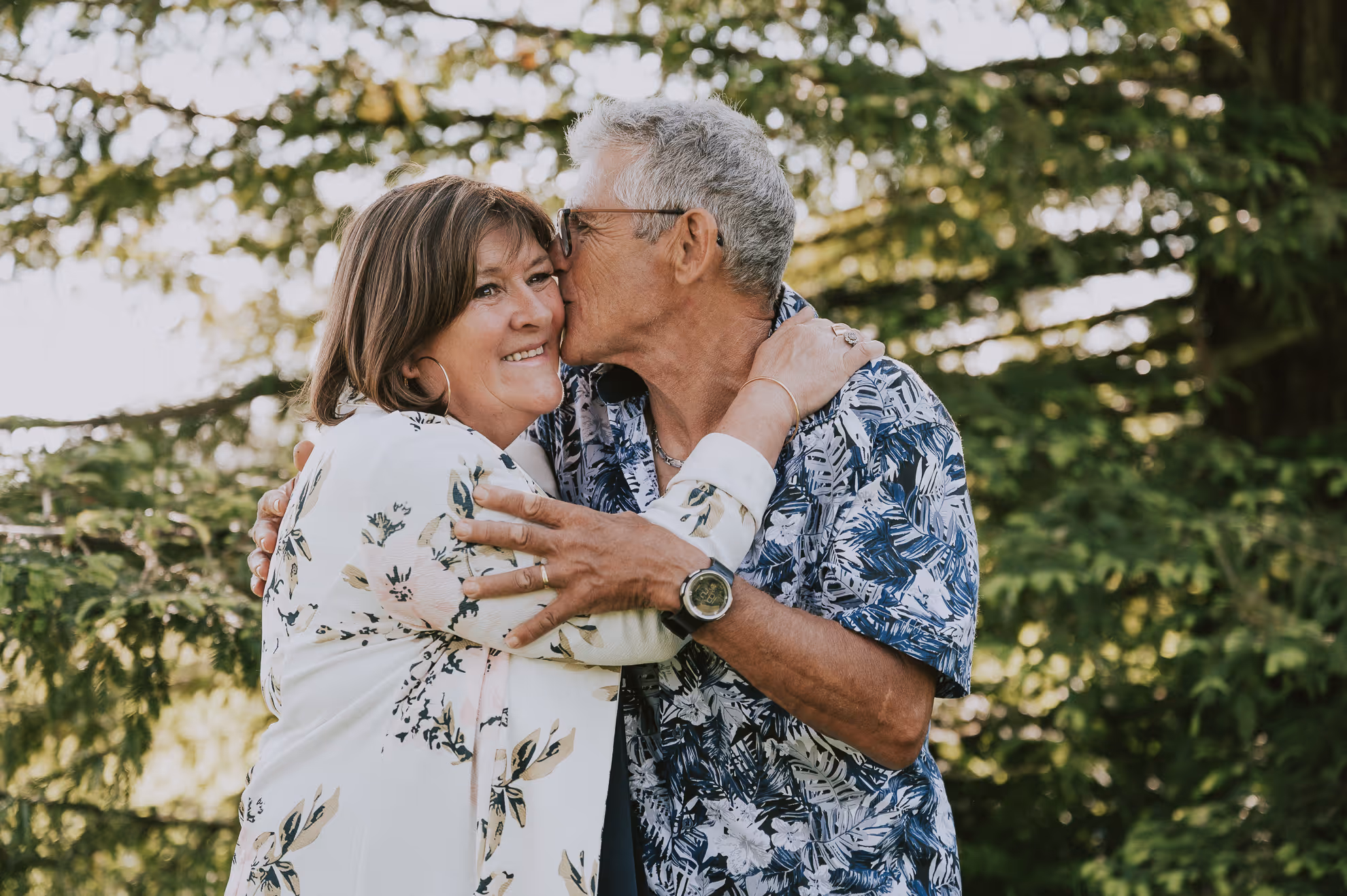 Un homme embrasse affectueusement une femme sur la joue dans un parc verdoyant.