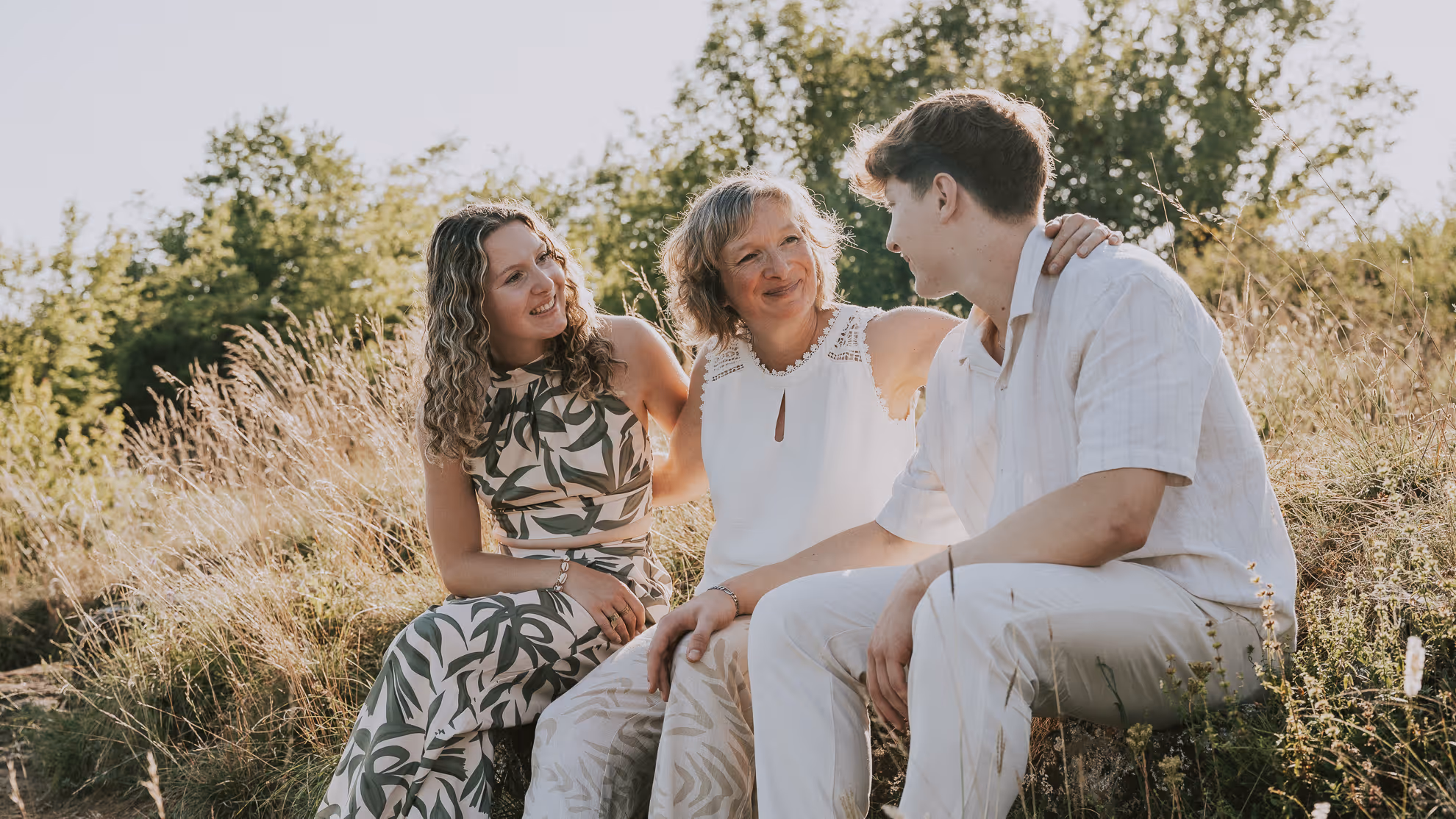 Quatre personnes en plein air sur un rocher, avec un homme embrassant une femme debout, une jeune femme assise souriante, et un jeune homme assis regardant vers eux.
