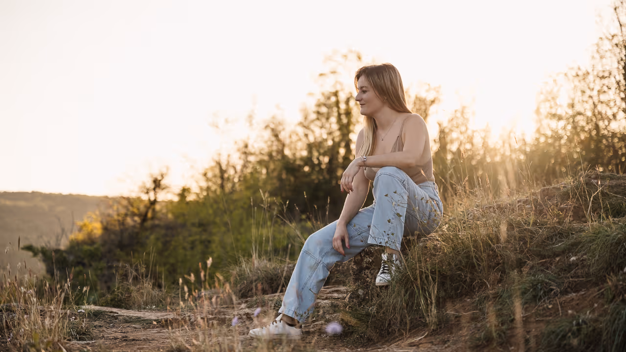 Jeune femme assise sur un rocher dans un champ à la lumière du coucher du soleil.