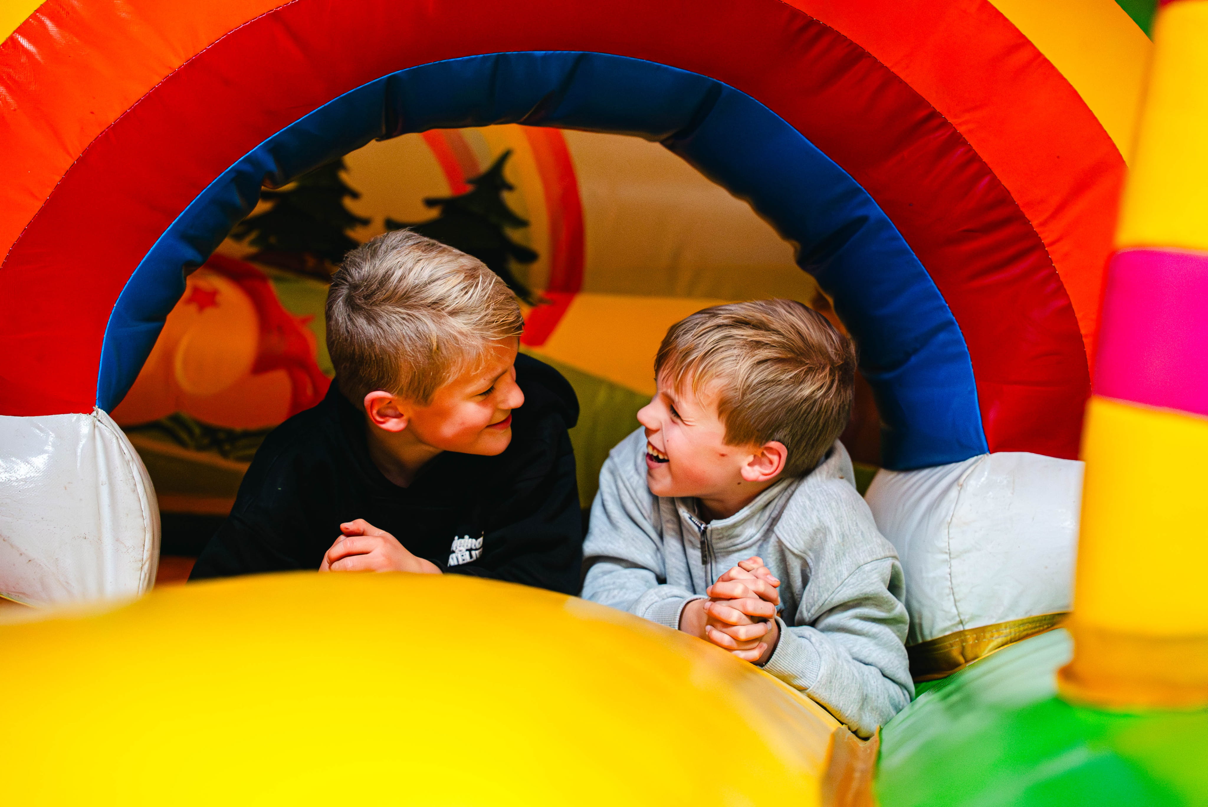 Twee jonge jongens die samen lachen terwijl ze binnen in een kleurrijk springkasteel liggen.