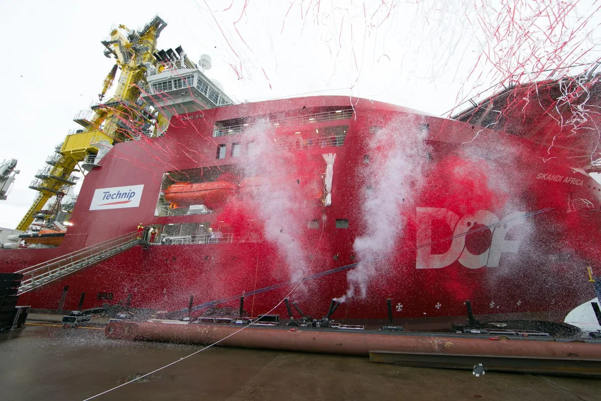 Scheepsdoop: een fles knalt stuk tegen de rode romp van een nieuw schip
