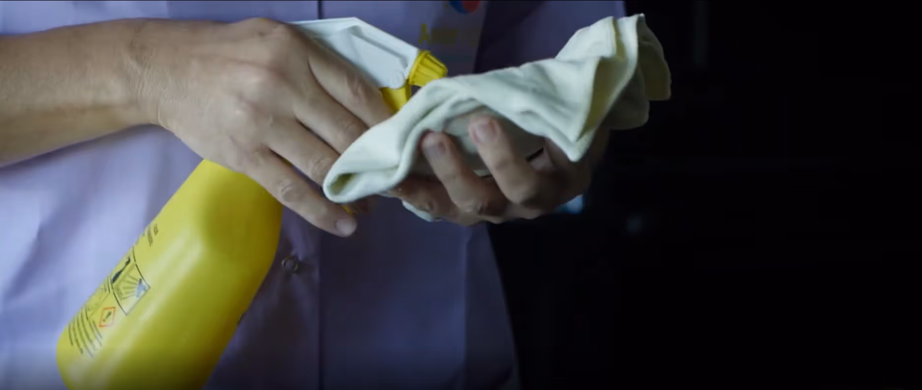 Une personne tenant un chiffon et un spray jaune de produit nettoyant.