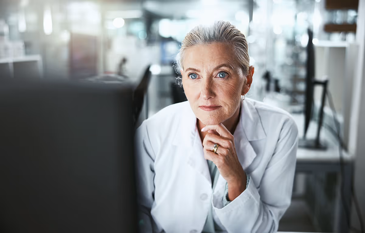 Scientist in a lab coat looks at a computer screen in a laboratory.