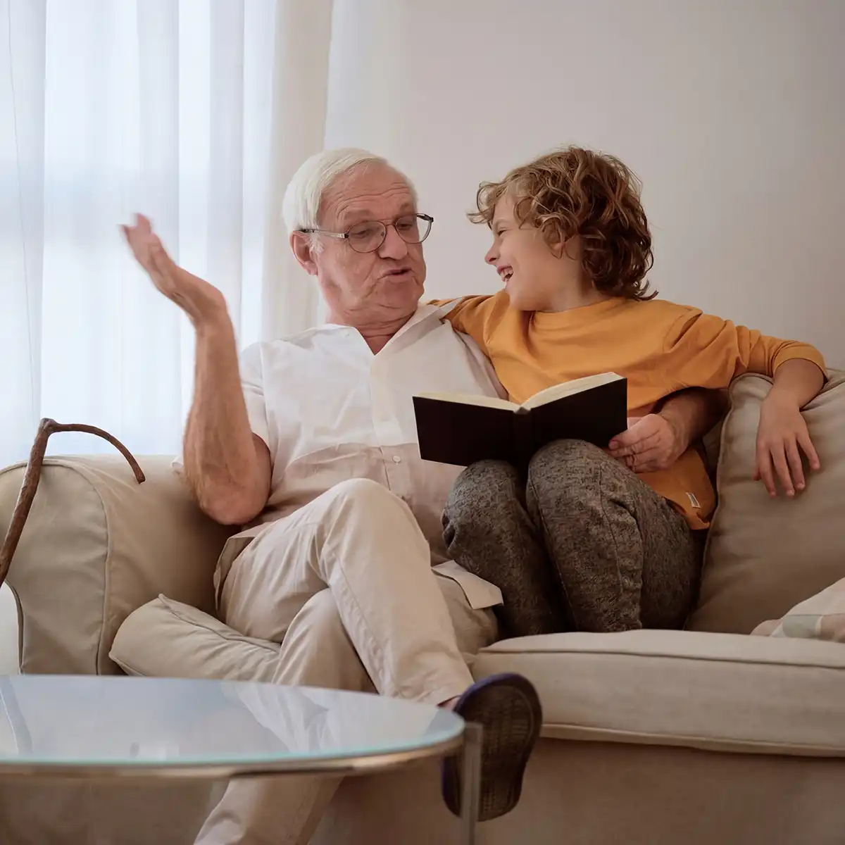 Oudere man leest een boek voor aan een lachende jongen terwijl ze samen op een bank zitten.