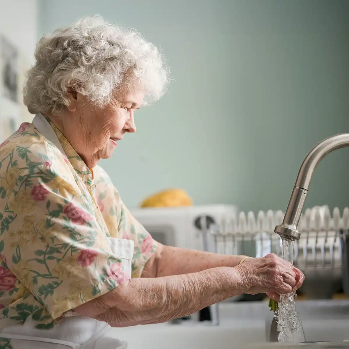 Oudere vrouw wast groenten onder stromend water in de keuken.