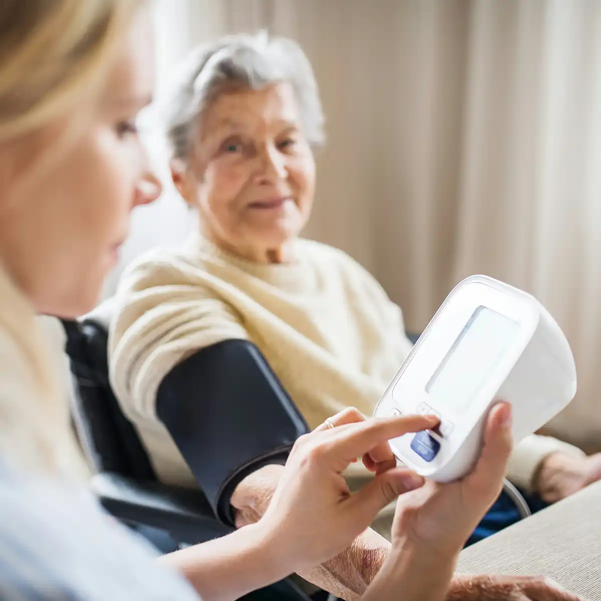 Zorgverlener meet de bloeddruk van een oudere vrouw met een digitale bloeddrukmeter.
