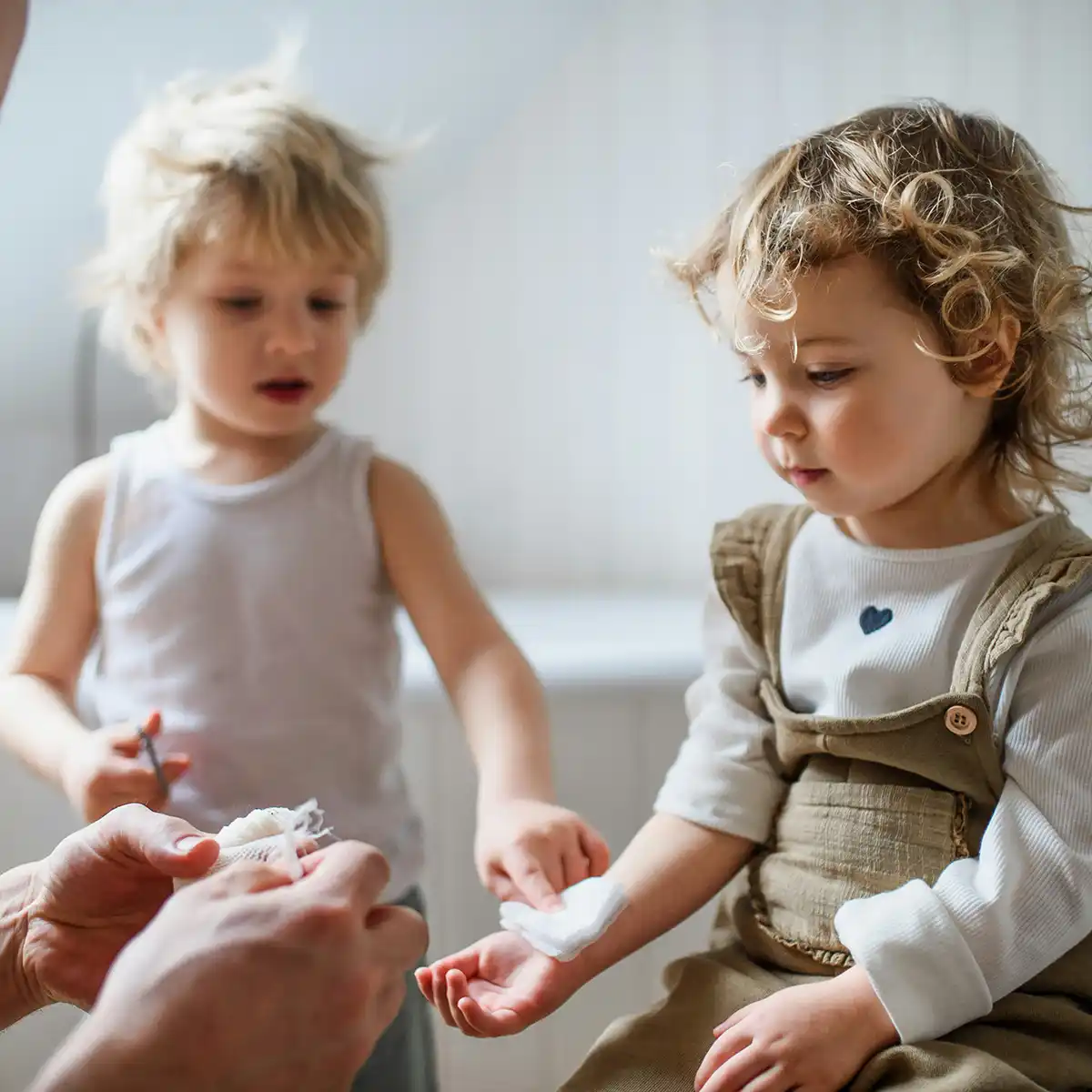 Een volwassene verzorgt de arm van een jong kind met een verband terwijl een ander kind toekijkt.